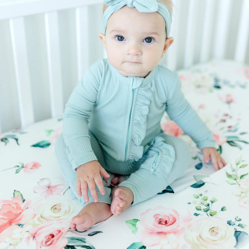 Baby sitting on peach floral fitted crib sheet in a crib.
