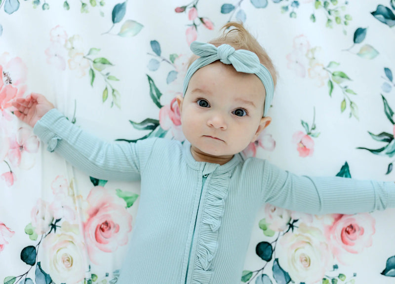 Baby lying on fitted crib sheet with peach floral pattern.