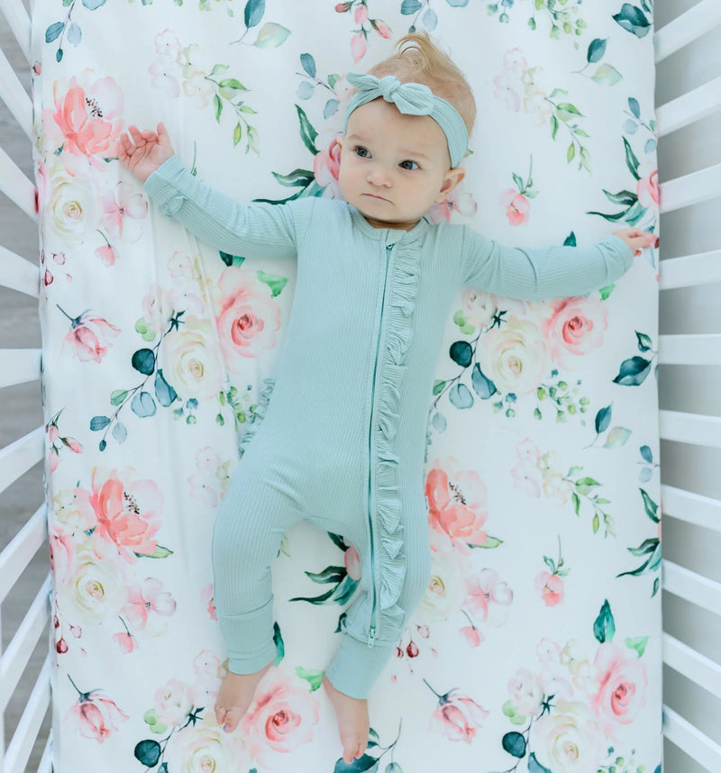 Fitted crib sheet with peach floral design in a crib with baby lying on it.