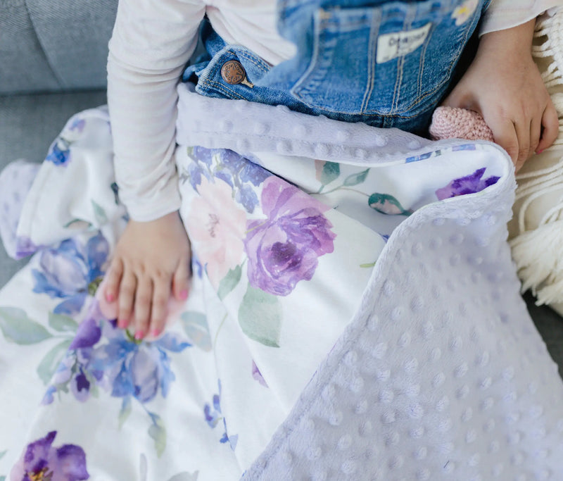Premium baby and toddler blanket with purple and blush floral design, minky dot texture, and child wrapped in it.
