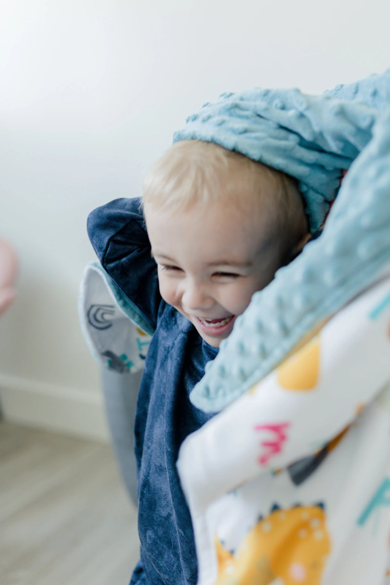 Baby smiling while wrapped in blue dino-themed minky blanket.
