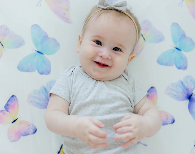 Baby lying on a fitted crib sheet with colorful butterfly pattern.