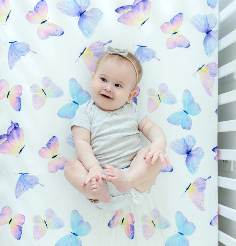 Butterfly-patterned fitted crib sheet with baby sitting on it.