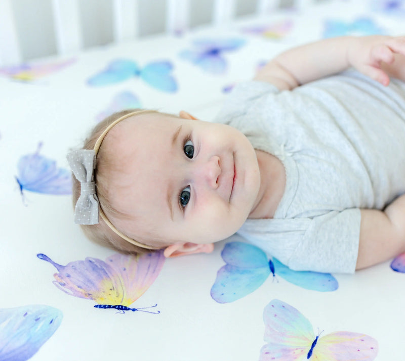 Baby lying on fitted crib sheet with butterfly pattern, made of soft rayon and spandex.