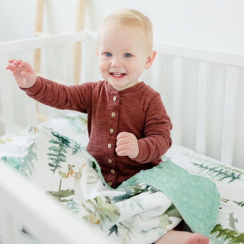 Baby wrapped in "In The Woods" minky blanket with forest design.