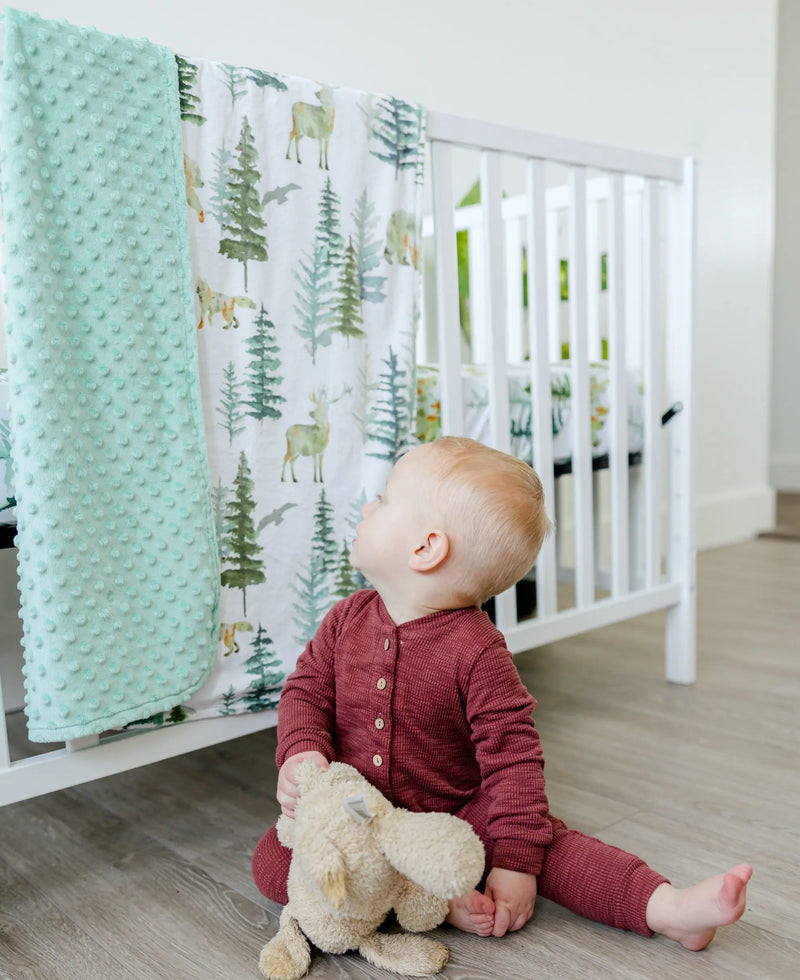 Baby looking at 'In The Woods' minky blanket draped over crib.