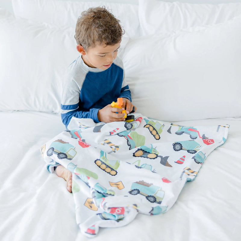 Boy with construction truck patterned minky blanket on bed.