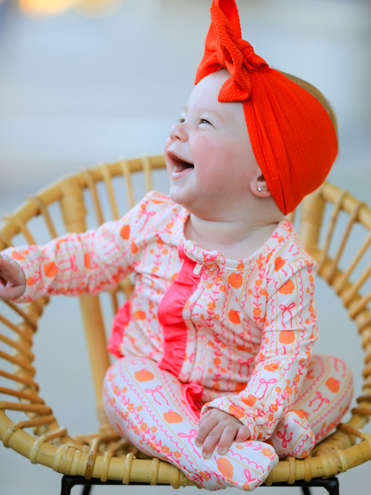 Baby zip sleeper in pumpkin and bow stripe print with bright pink ruffle trim and front zipper closure