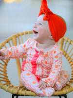 Baby zip sleeper in pumpkin and bow stripe print with bright pink ruffle trim and front zipper closure
