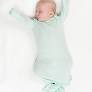 Baby in a light green onesie with long sleeves and legs, lying on a white blanket.
