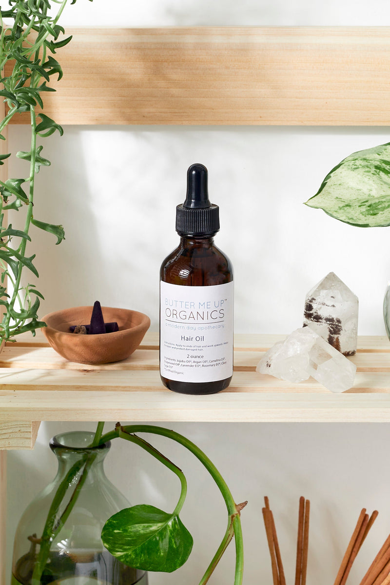 Organic Hair Oil in glass bottle on wooden shelf with plants and crystals.