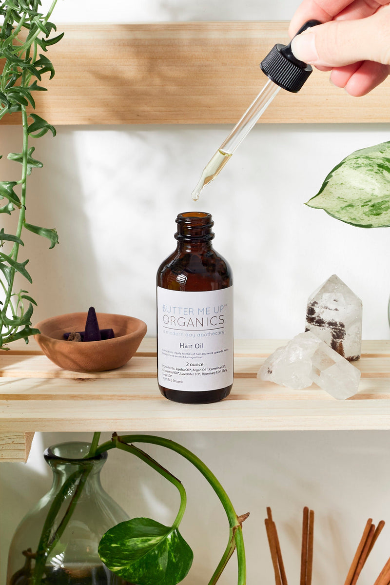 Organic Hair Oil bottle with dropper on a wooden shelf, surrounded by plants and crystals.