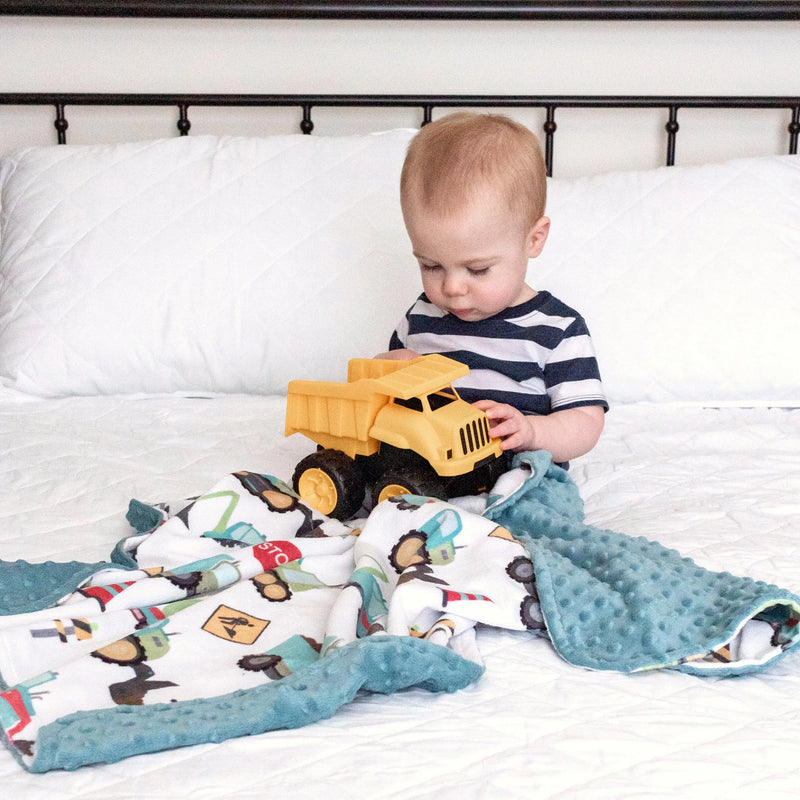 Baby playing with yellow truck on construction-themed minky blanket.