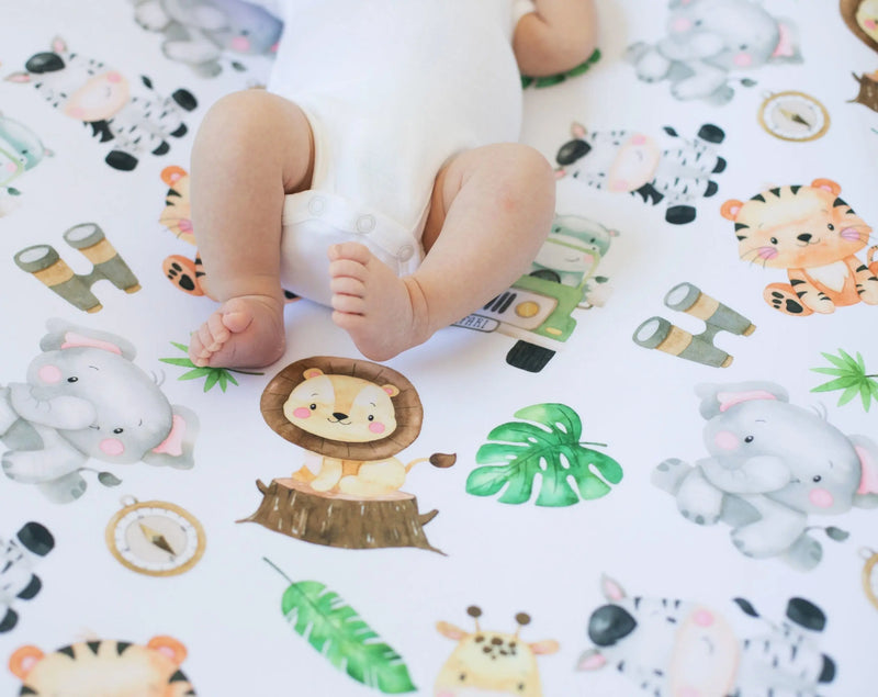 Safari themed fitted crib sheet with colorful animal illustrations and a baby lying on it.