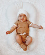 Caramel organic cotton baby bodysuit with contrasting natural trim, shoulder snaps, and leg snaps.
