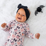 Footie pajamas in pink polka dot print with a matching bow headband, shown with a full-length zipper