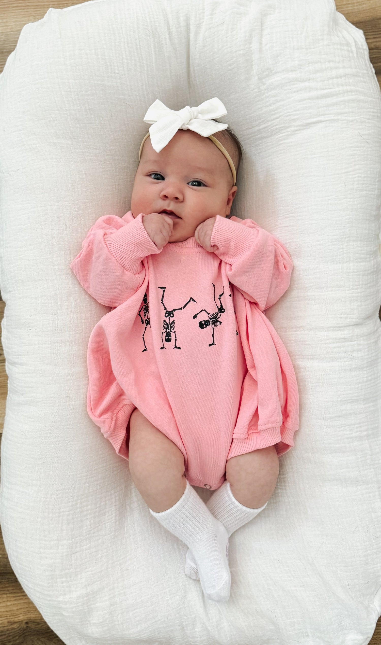 Pink long-sleeve sweatshirt romper with a screenprinted dancing skeletons graphic