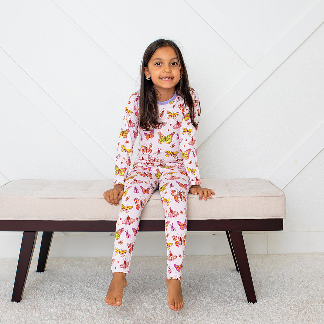 Two-piece long-sleeve pink ButterBloom pajama set with matching top and pants on a smiling child.