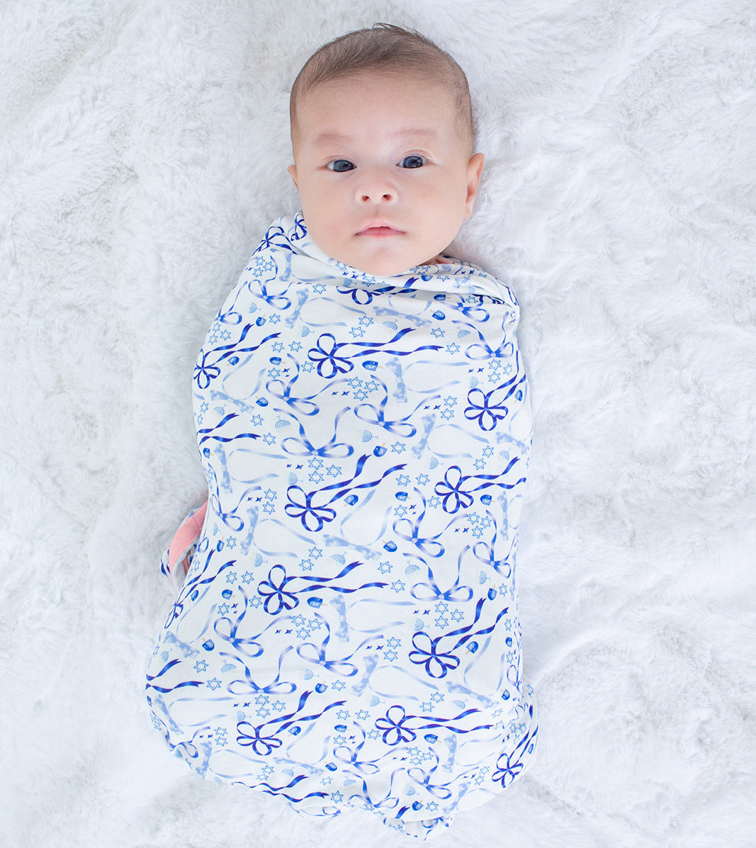 Swaddle blanket with blue bows, menorahs, Star of David and dreidels on a light background.