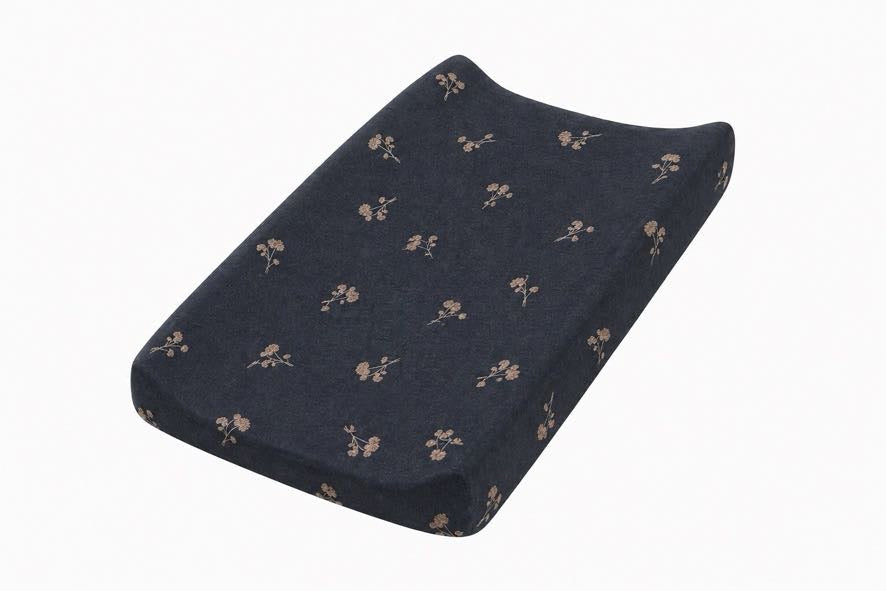 Changing pad cover in light blue with a small white dandelion print, fitted over a contoured changing pad