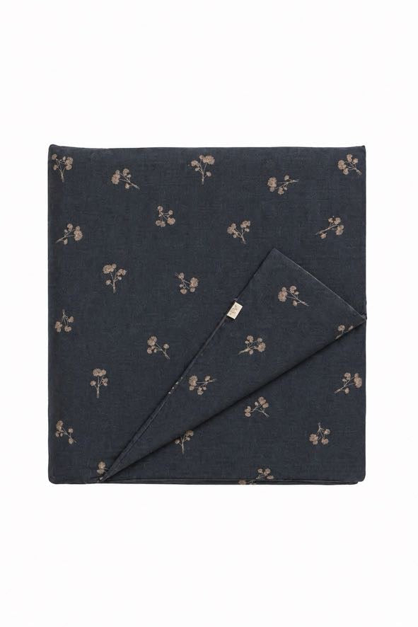 Quilted crib blanket with blue dandelion print on white cotton, hand-tufted stitching visible