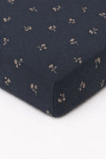 Crib sheet in white with a blue dandelion floral print, fitted over a standard crib mattress