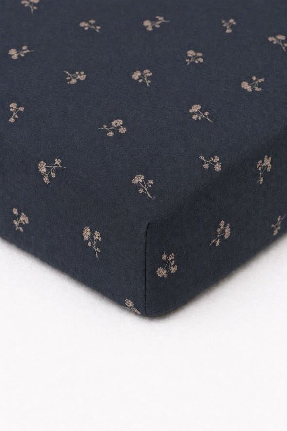 Crib sheet in white with a blue dandelion floral print, fitted over a standard crib mattress