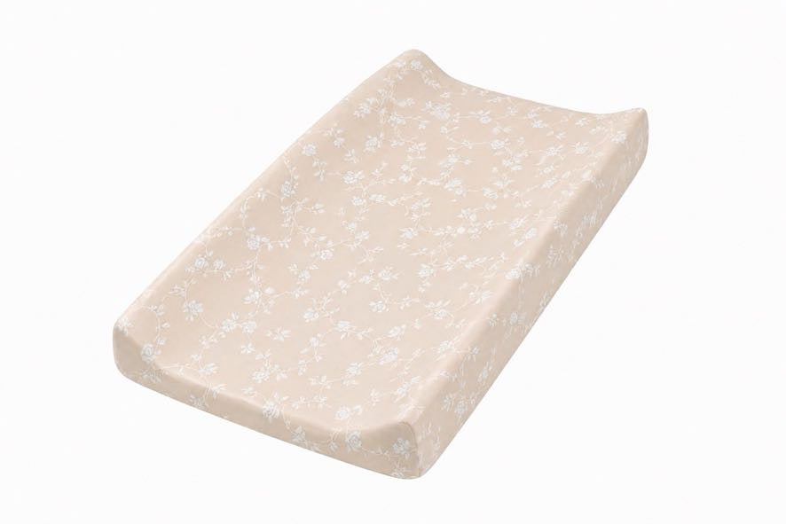 Beige changing pad cover with a white floral print, fitted over a contoured changing pad