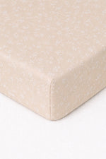 Crib sheet in beige with a white floral print, fitted on a standard crib mattress