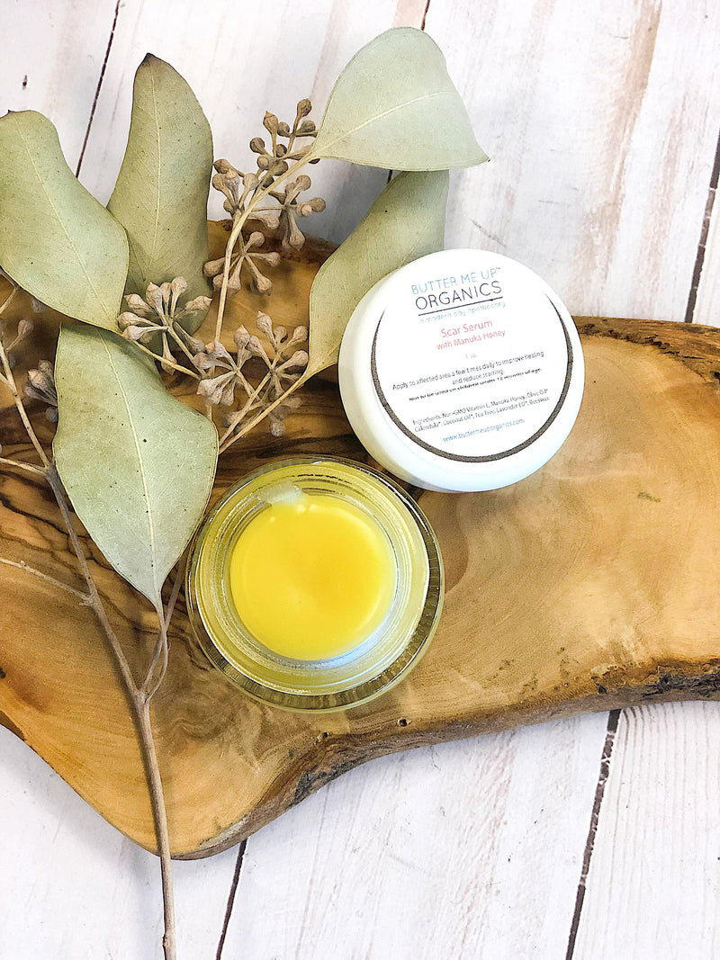 Scar serum in glass jar on wooden tray with natural leaves, showcasing ingredients like manuka honey and vitamin E.