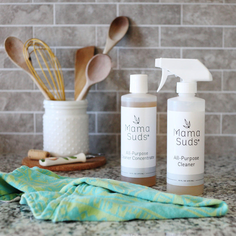 MamaSuds All-Purpose Cleaner Concentrate on kitchen counter with cleaning cloth and kitchen utensils.