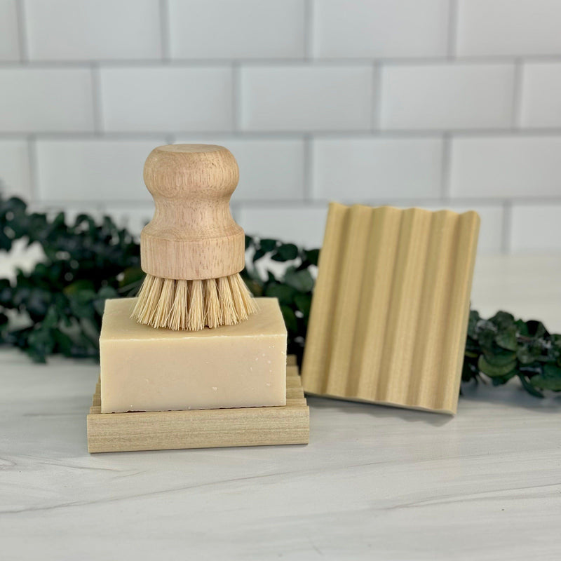Wooden ridged soap dish with bamboo brush and soap in a bathroom setting.