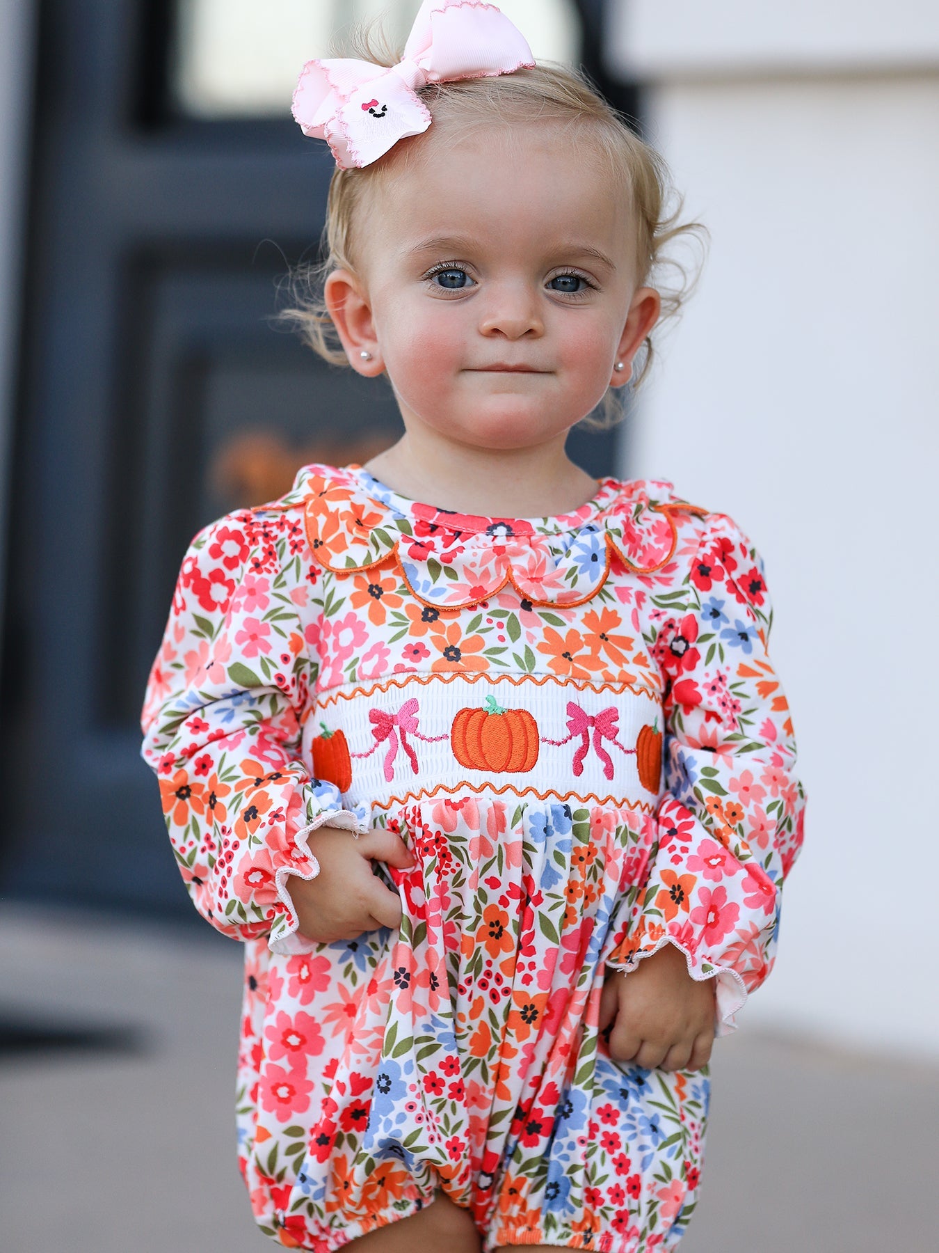 Baby girl romper with pumpkin embroidery, floral details, and a bow at the front in a smock cover-up style.