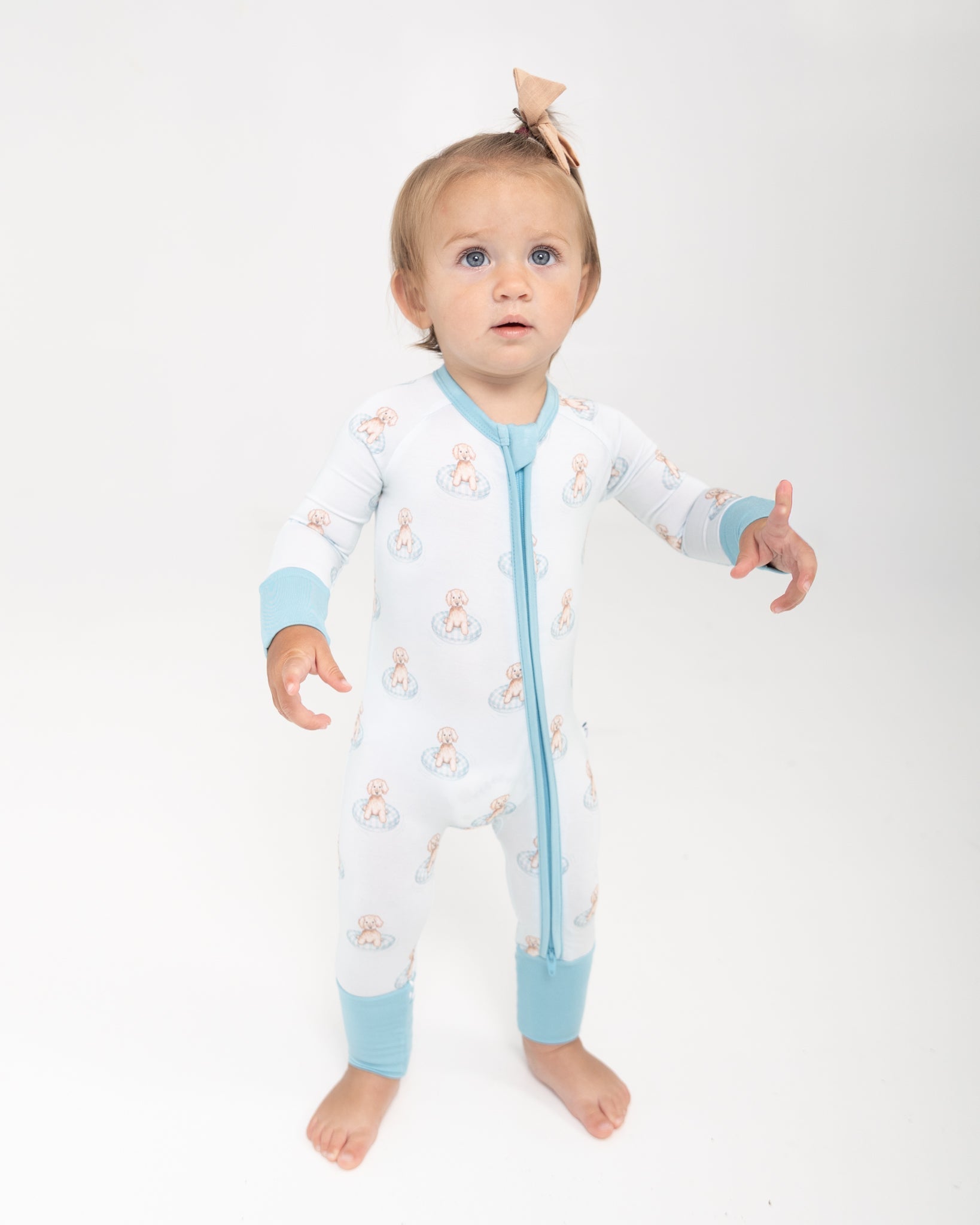 Baby zip-up pajamas with a print of puppies in little blue pools, featuring fold-over feet with grippers.