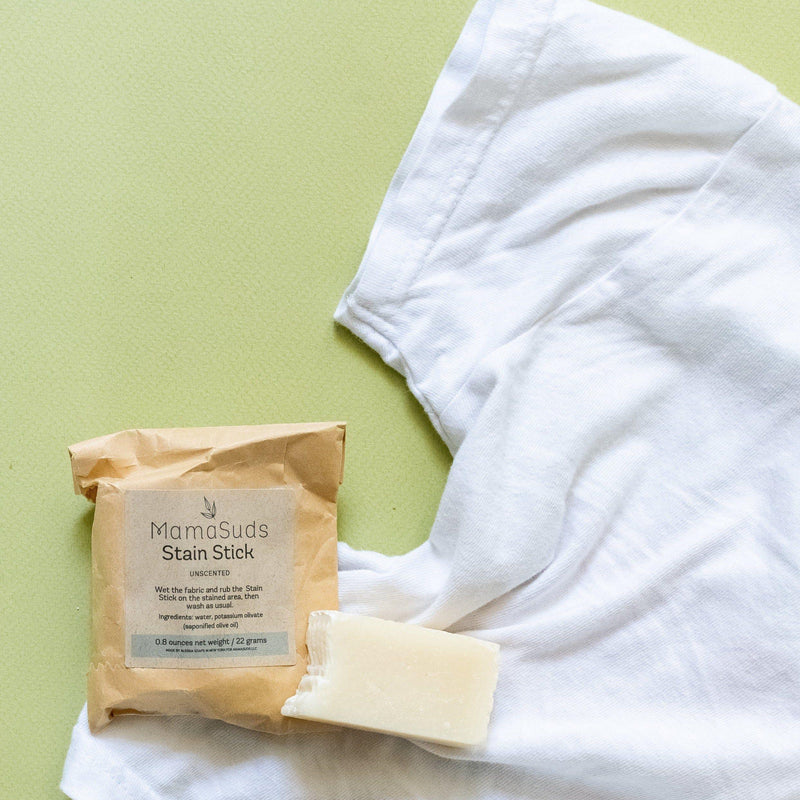 Laundry stain stick with packaging and a white shirt on a green surface.