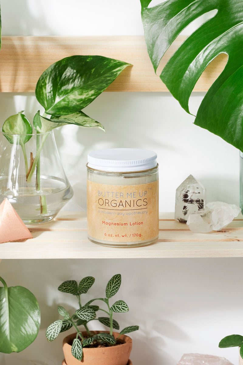 Organic Magnesium Lotion in a glass jar on a shelf surrounded by plants and crystals.