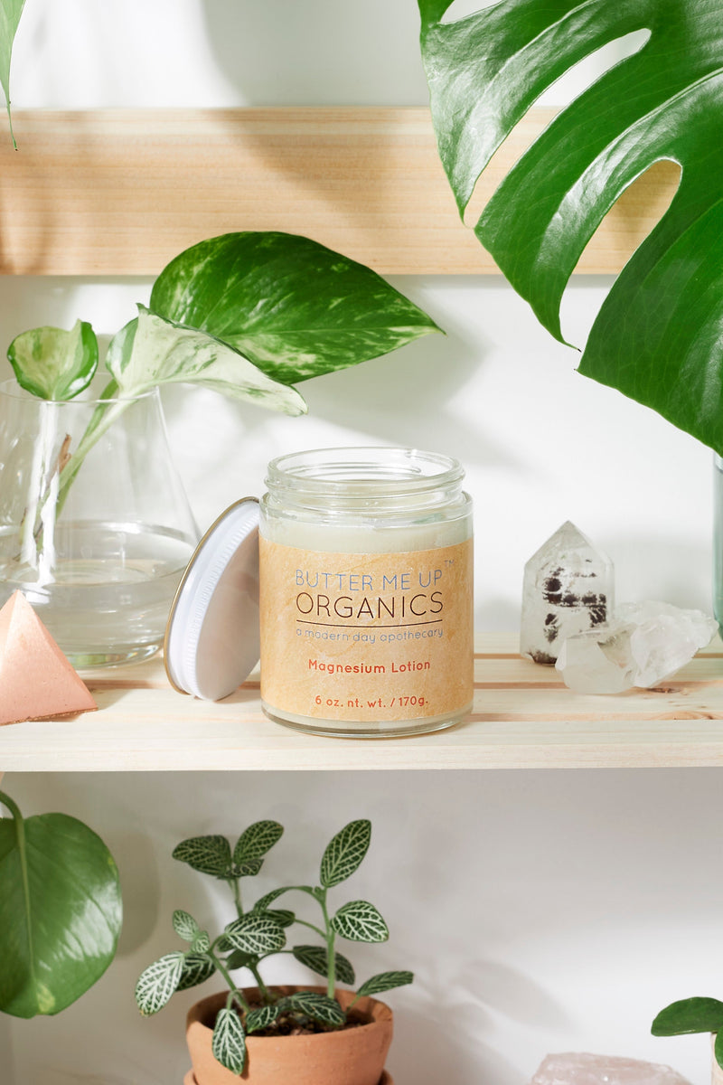 Organic Magnesium Lotion in glass jar on shelf with plants and crystals.