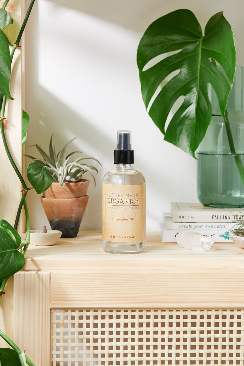 Magnesium Oil Spray in glass bottle on wooden shelf, surrounded by plants and natural decor.