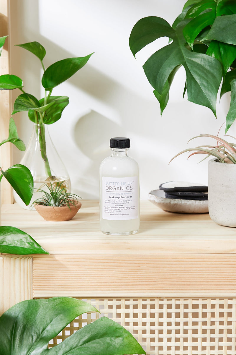 Organic Makeup Remover in recycled glass bottle on wooden shelf with plants, gentle for sensitive skin.