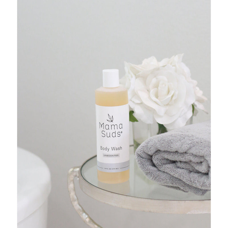 MamaSuds Body Wash Soap bottle with lavender or lemon scent option on a table alongside flowers and a towel, natural ingredients focus.