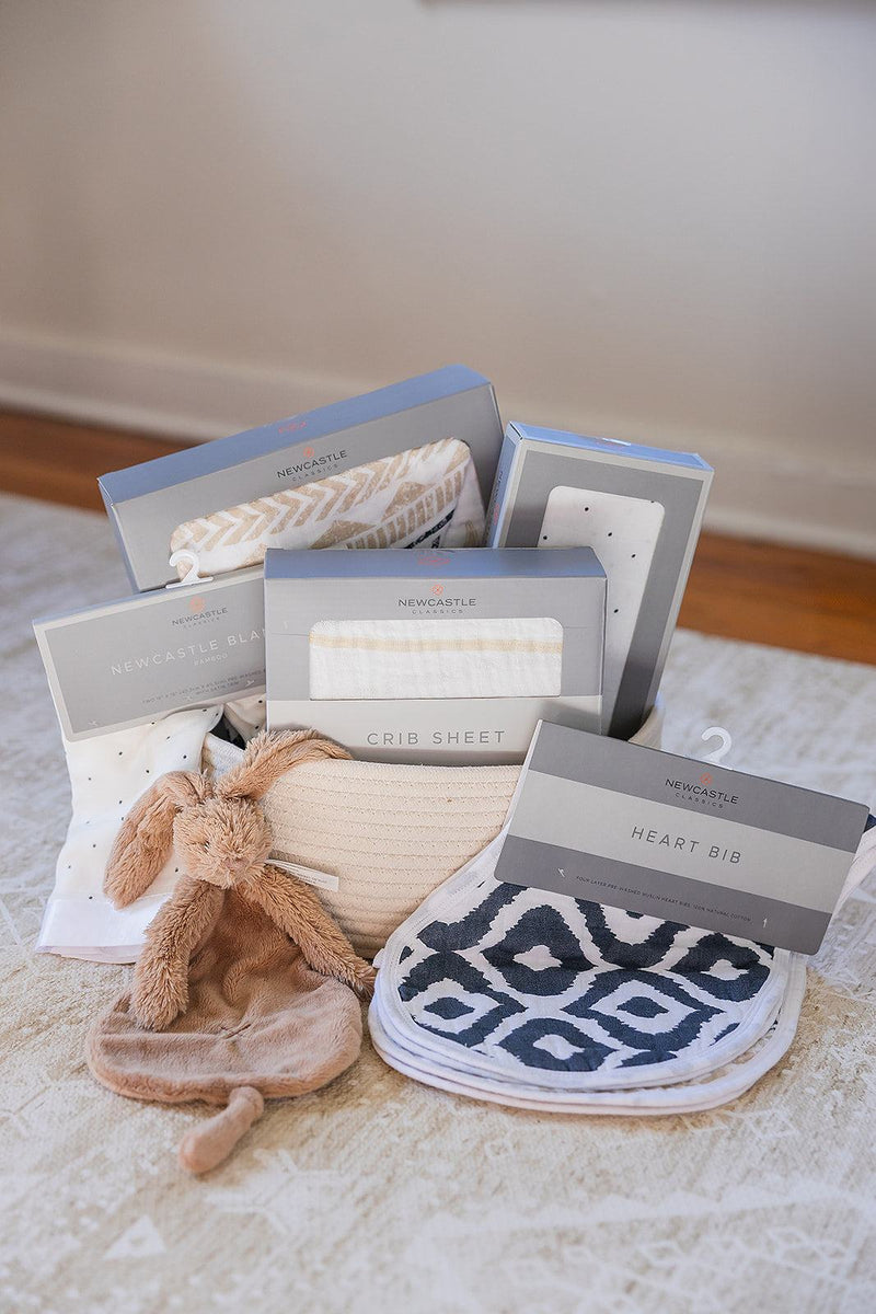 Welcome Baby basket with cotton blanket, bamboo swaddle, crib sheet, bib set, and Rabbit Richie tuttle in a rope basket.