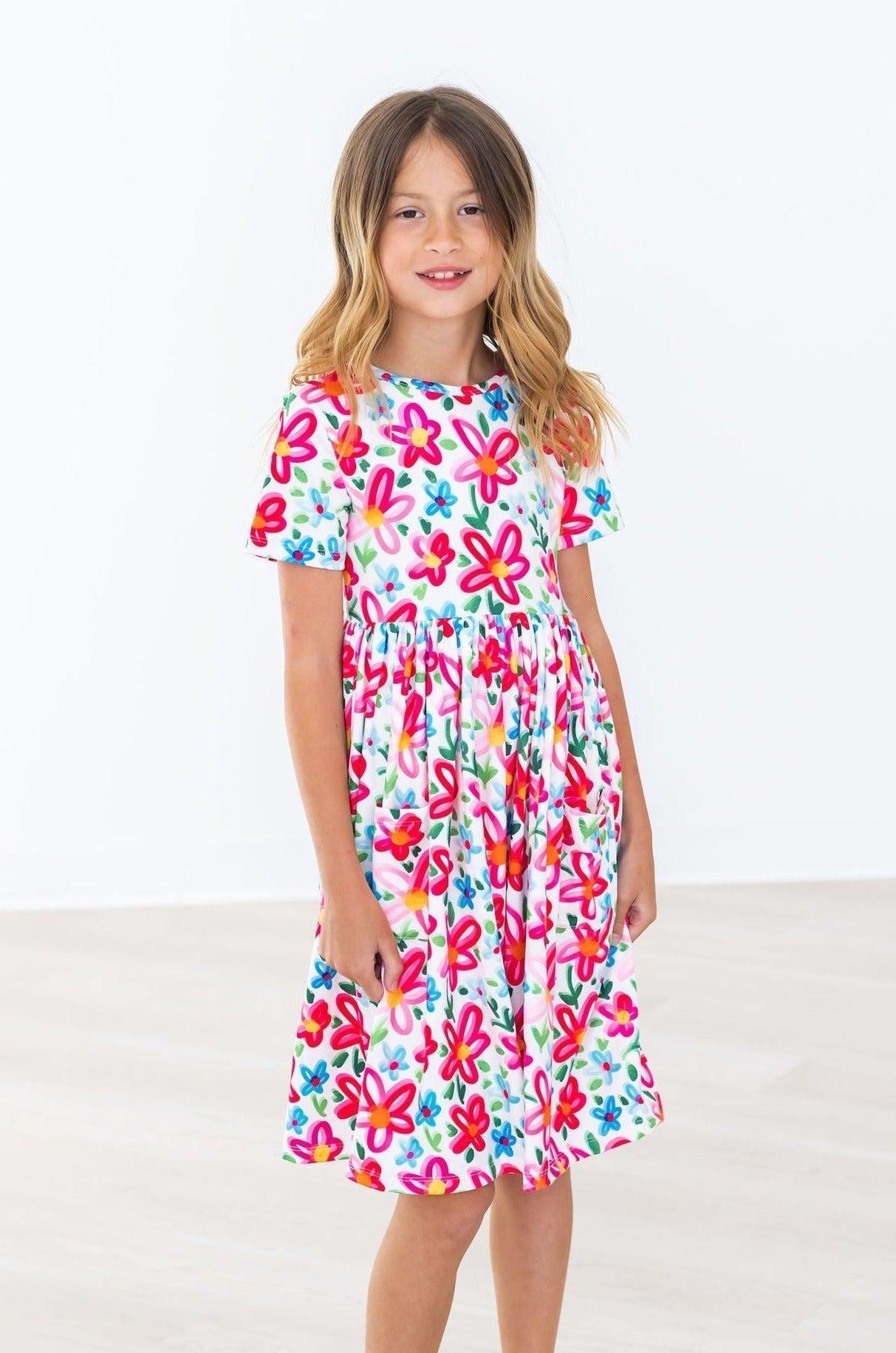 Mila & Rose baby girl in a vibrant neon floral short sleeve twirl dress with pockets, playing happily.