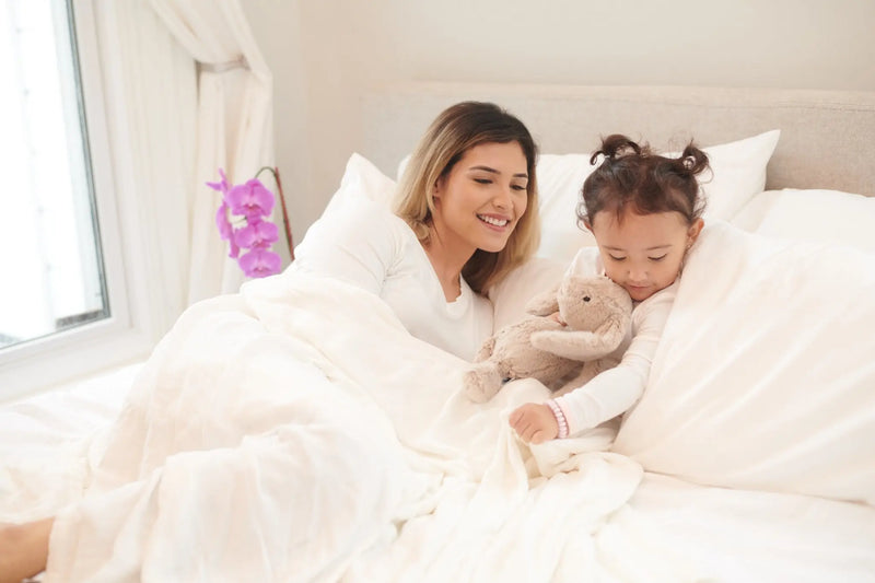 Pristine White oversized bamboo muslin blanket on bed with mother and child.