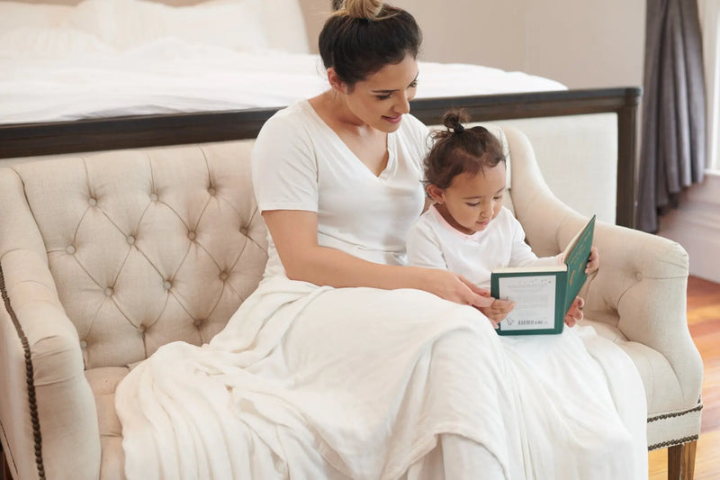 Pristine White Oversized King Luxury Bamboo Muslin Bed Blanket draped on couch with parent and child reading.