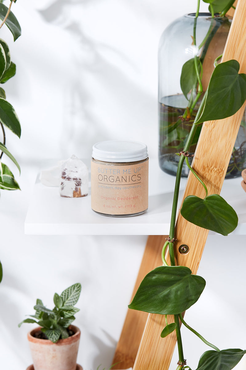 Organic deodorant in a clear glass jar on a white shelf with plants.