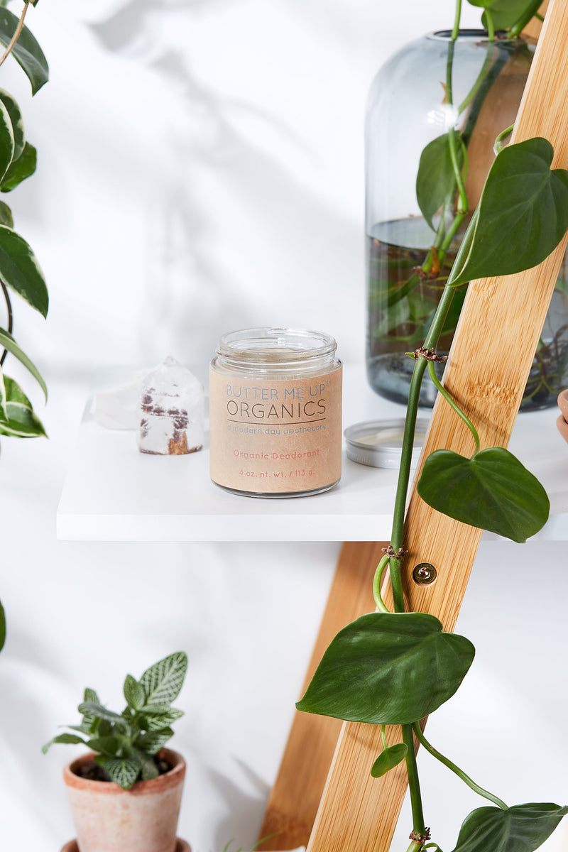 Organic deodorant in glass jar on shelf with plants.