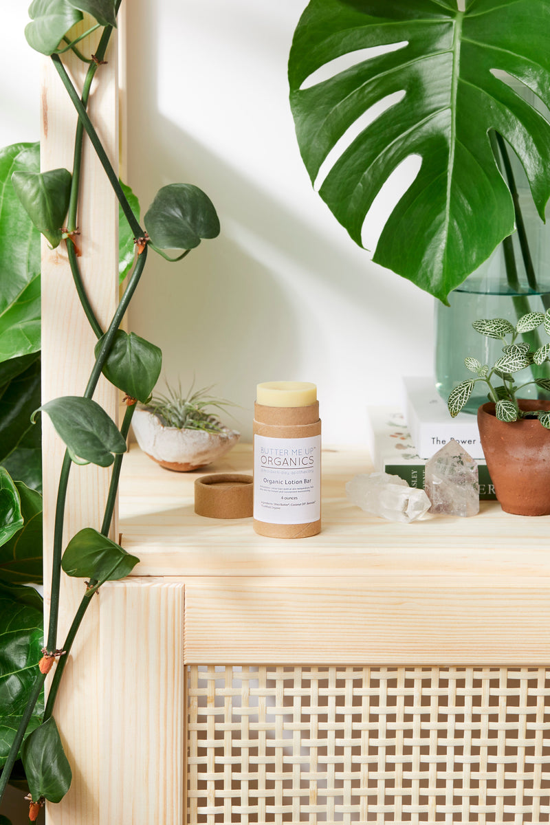 Organic lotion bar with shea butter and coconut oil on wooden surface, surrounded by plants.