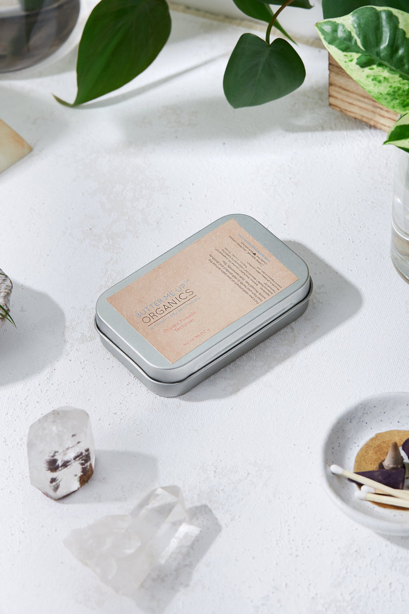 Organic pomade hair wax tin on a white surface with natural decor around.