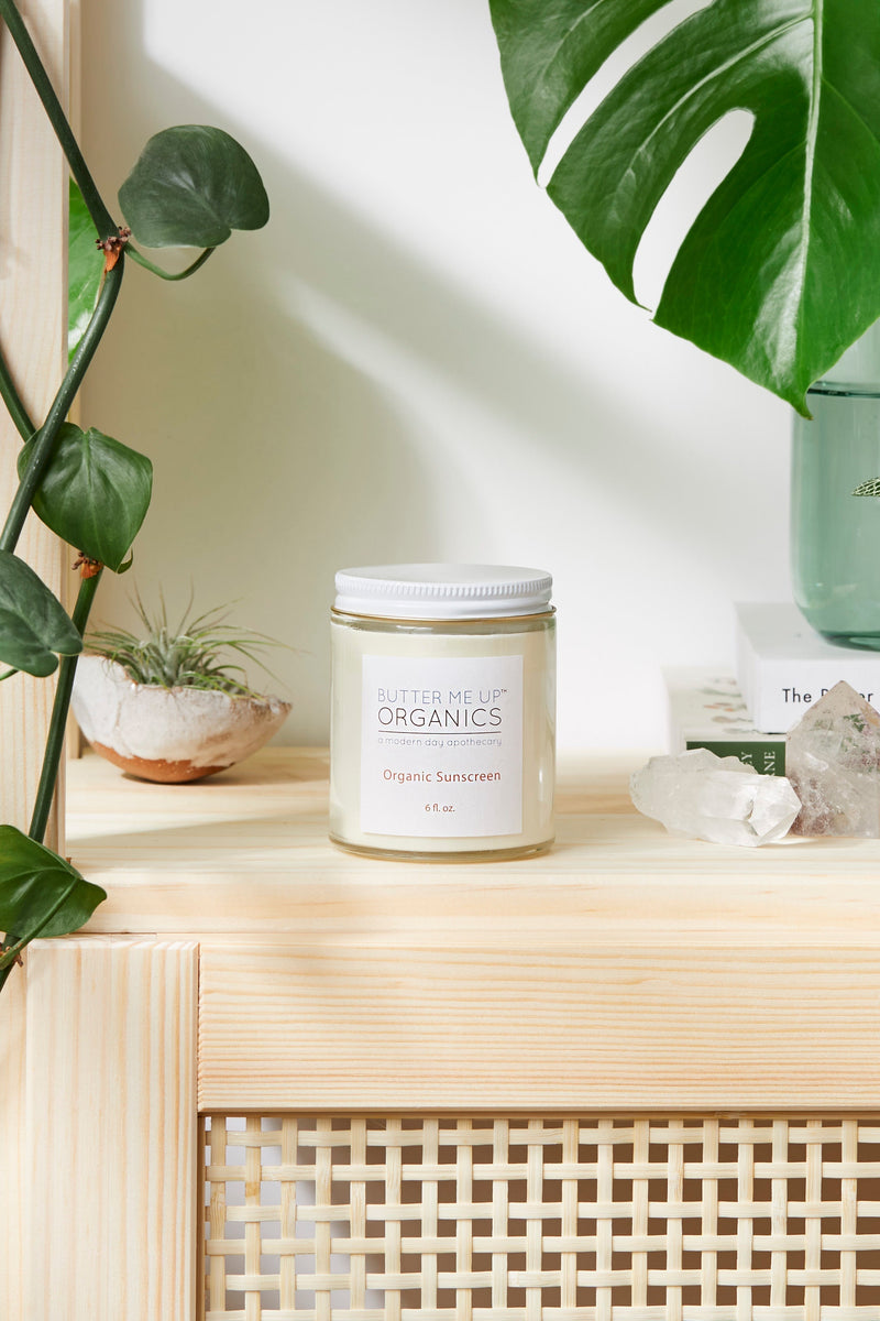 Organic sunscreen jar with non-nano zinc oxide on a shelf surrounded by plants and stones.