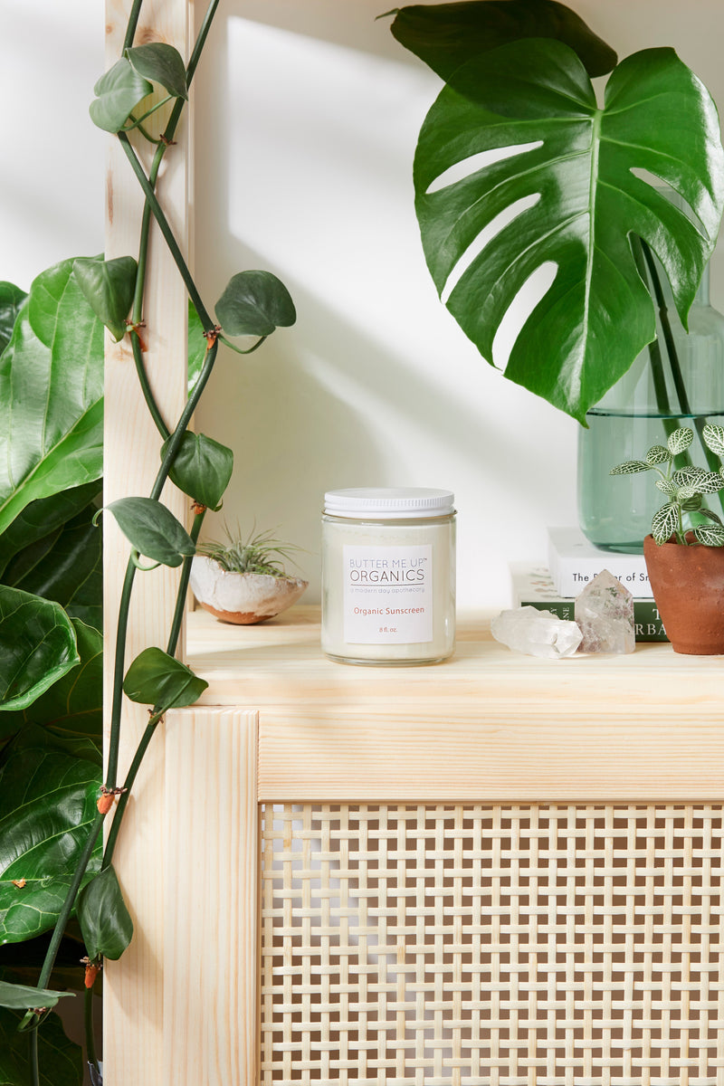 Natural organic sunscreen jar by Butter Me Up Organics on a wooden shelf with plants, featuring non-nano zinc oxide for safe sun protection.